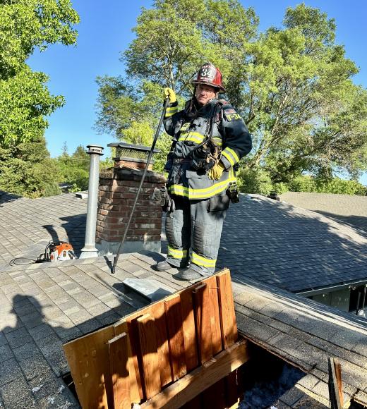 Steve Dunn, in his firefighting gear, stands on top of a roof.