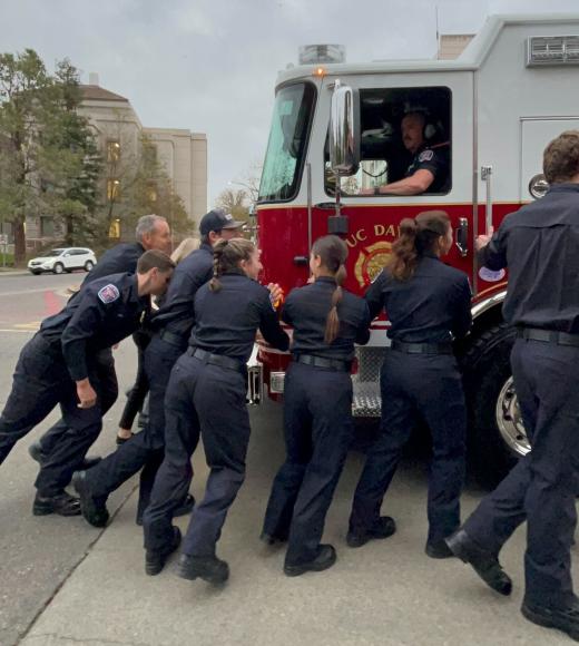 Side view of the Fire Truck being pushed in the garage by Firefighters. A firefighter sits behind the wheel, helping navigate the truck inside.