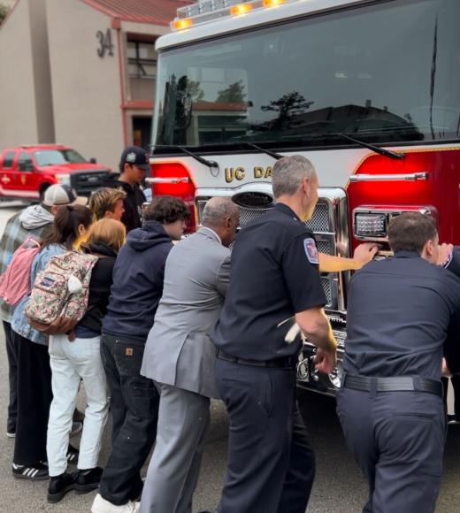 Community members, Chancellor Gary May, and Firefighters push the front of the new Fire Truck into Station 34.