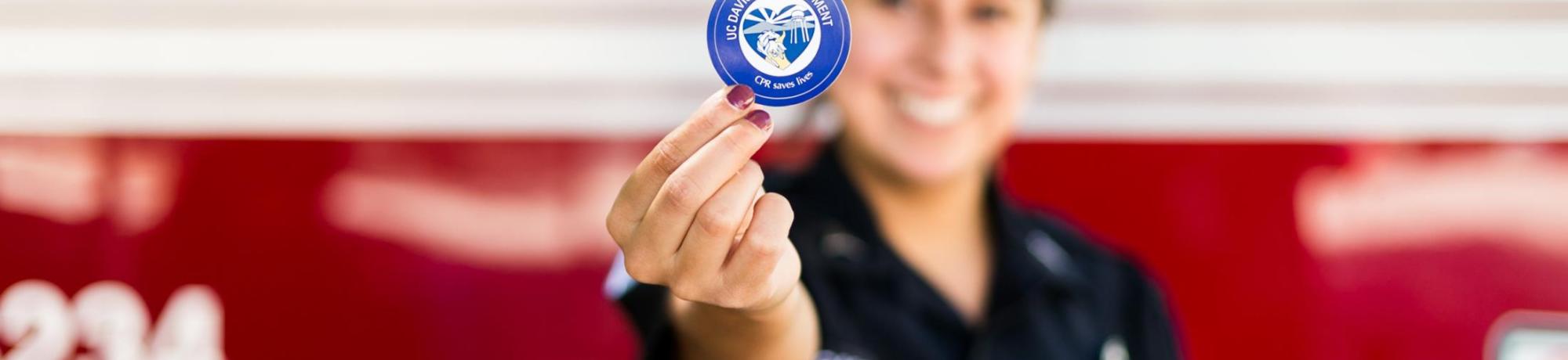 UC Davis Student EMT holding a CPR certification sticker.