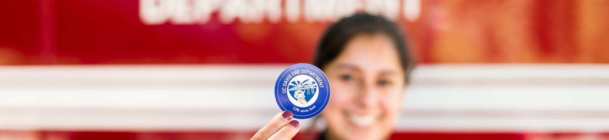 UC Davis Student EMT holding a CPR certification sticker.